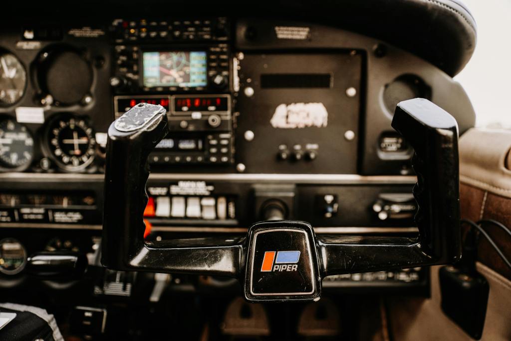Detailed image of an aircraft cockpit showing controls and instrumentation inside a Piper aircraft.